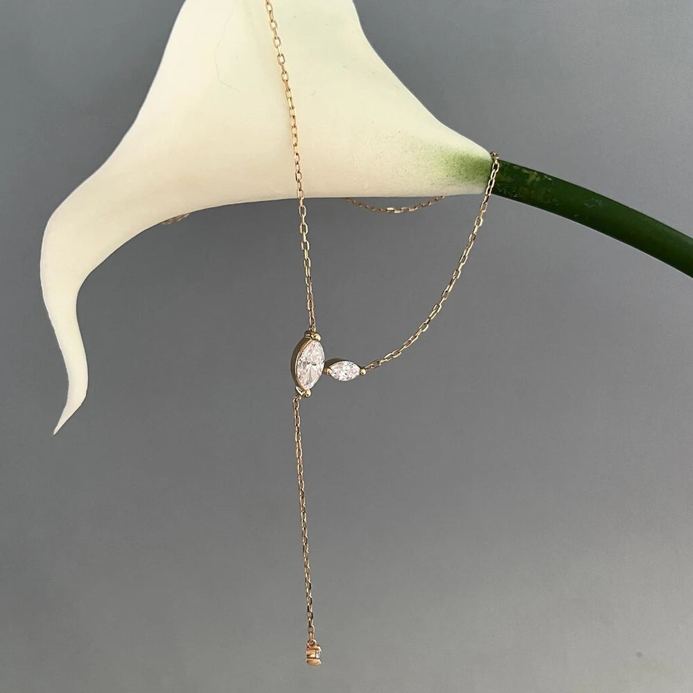 Gold necklace with a pendant on a white flower against a gray background