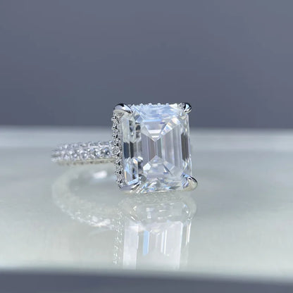 Diamond ring with a square-cut gemstone on a reflective surface with a gray background