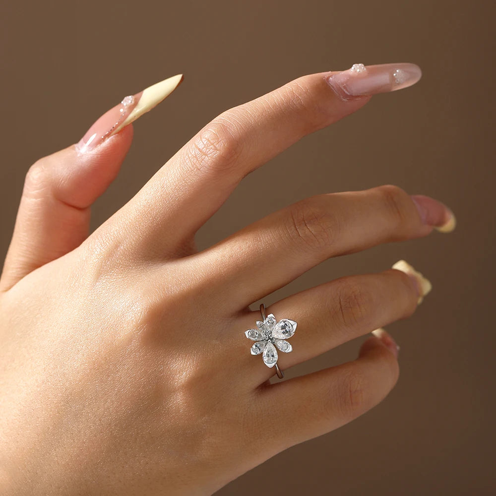 Hand wearing a silver ring with a flower design on a brown background