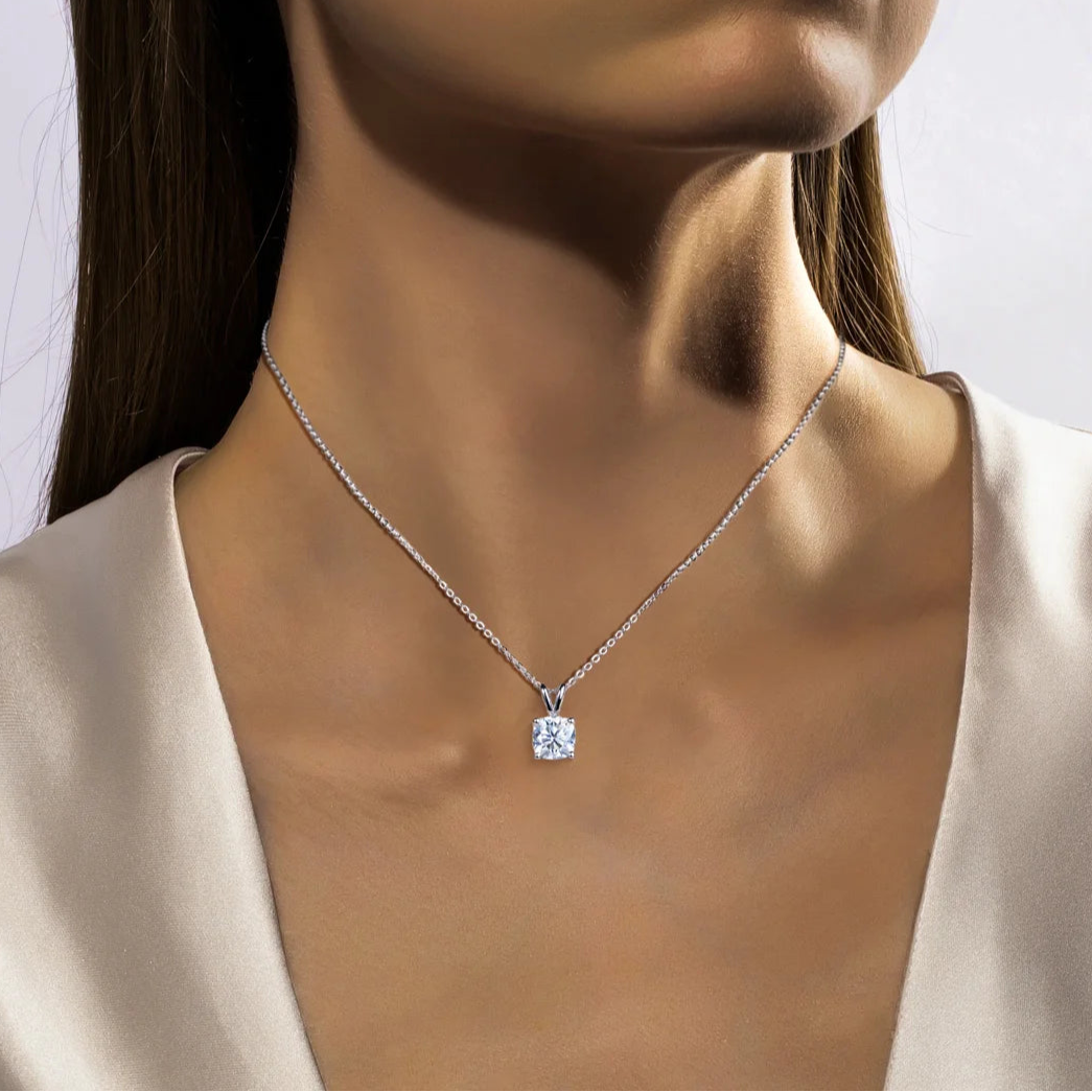 Woman wearing a silver necklace with a diamond pendant on a plain background