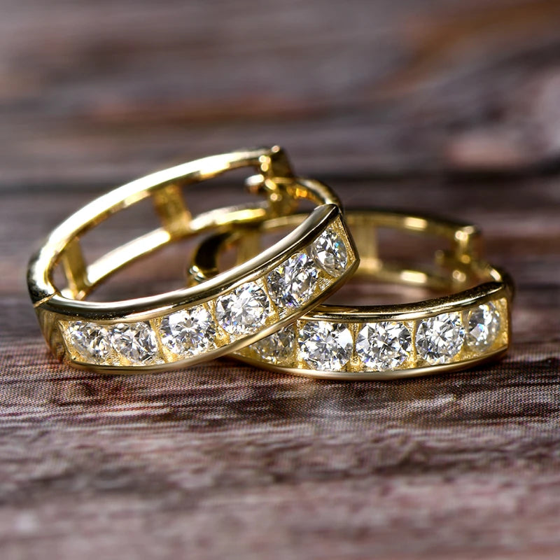 Two gold hoop earrings with clear gemstones on a wooden surface