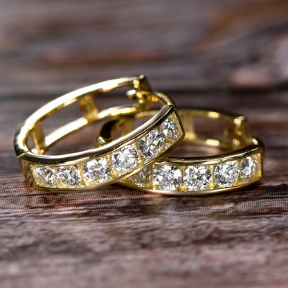 Two gold hoop earrings with clear gemstones on a wooden surface