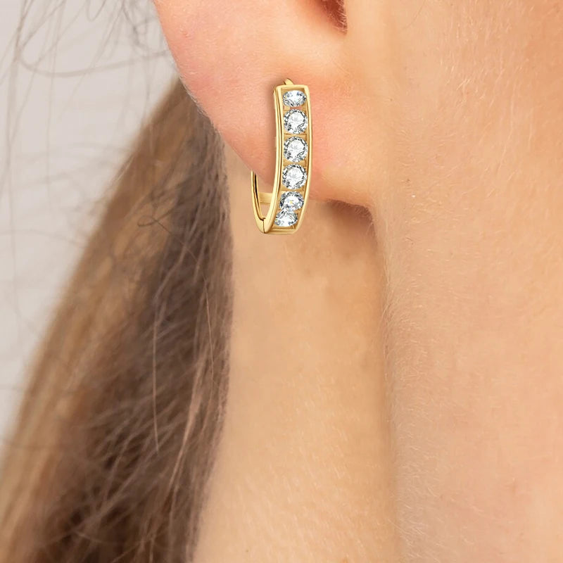 Gold hoop earring with embedded stones worn by a person.