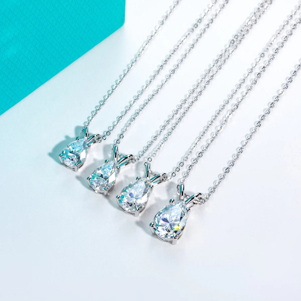 Set of silver necklaces with teardrop-shaped gemstones on a light blue background