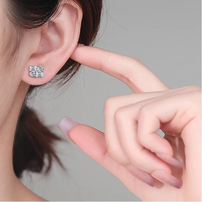Person wearing a diamond stud earring with a hand pointing to it.