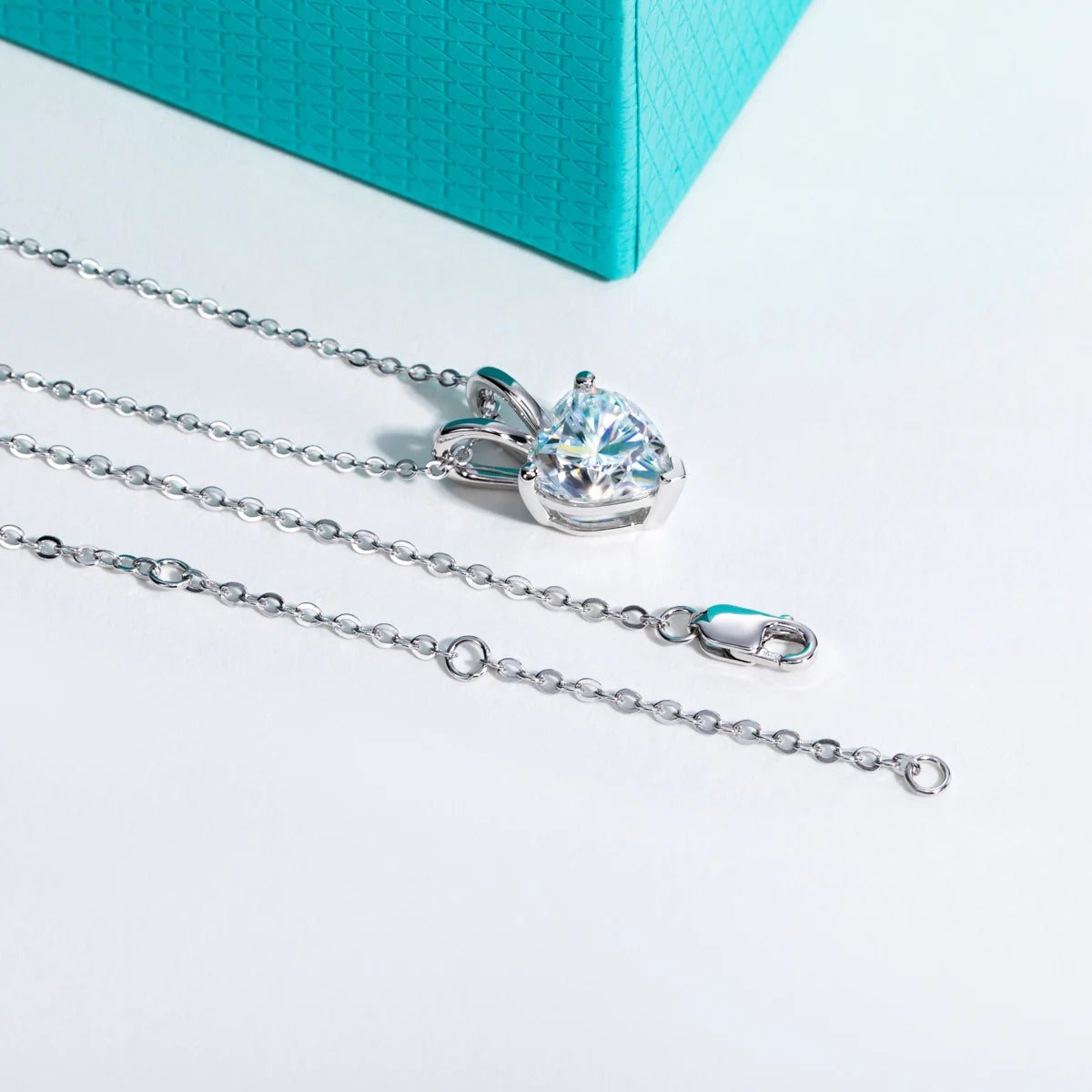 Heart-shaped diamond pendant on a silver chain with a turquoise box in the background