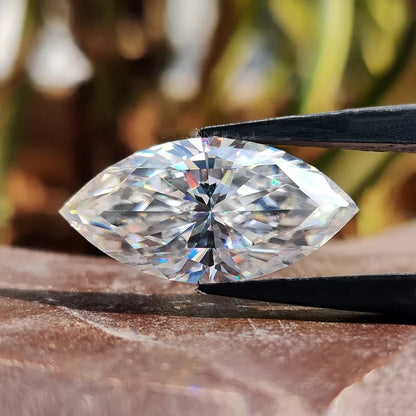 Marquise-shaped diamond held by tweezers with a blurred natural background
