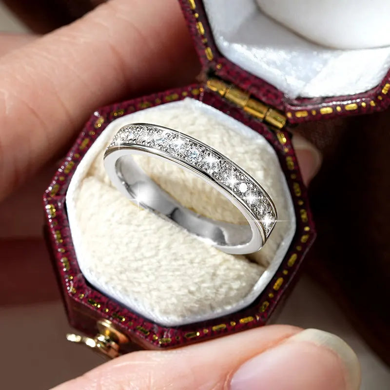 Silver ring with diamonds in a decorative box held by a hand.