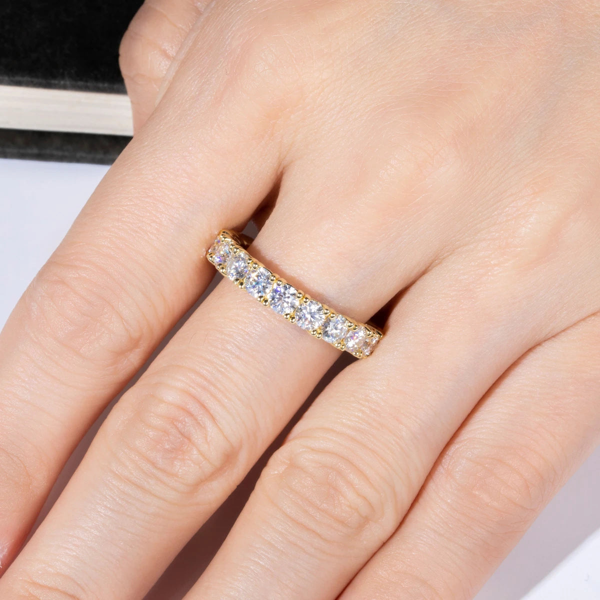 Gold ring with diamonds on a person's finger against a neutral background