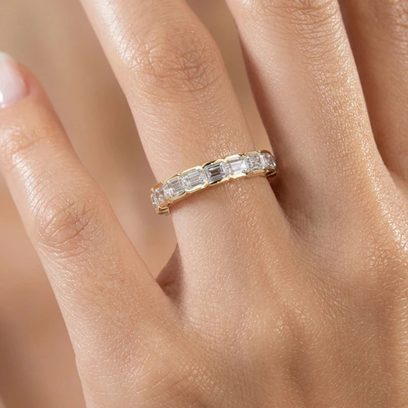 Gold ring with diamonds on a person's finger against a neutral background