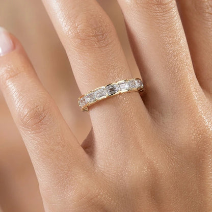 Gold ring with diamonds on a person's finger against a neutral background