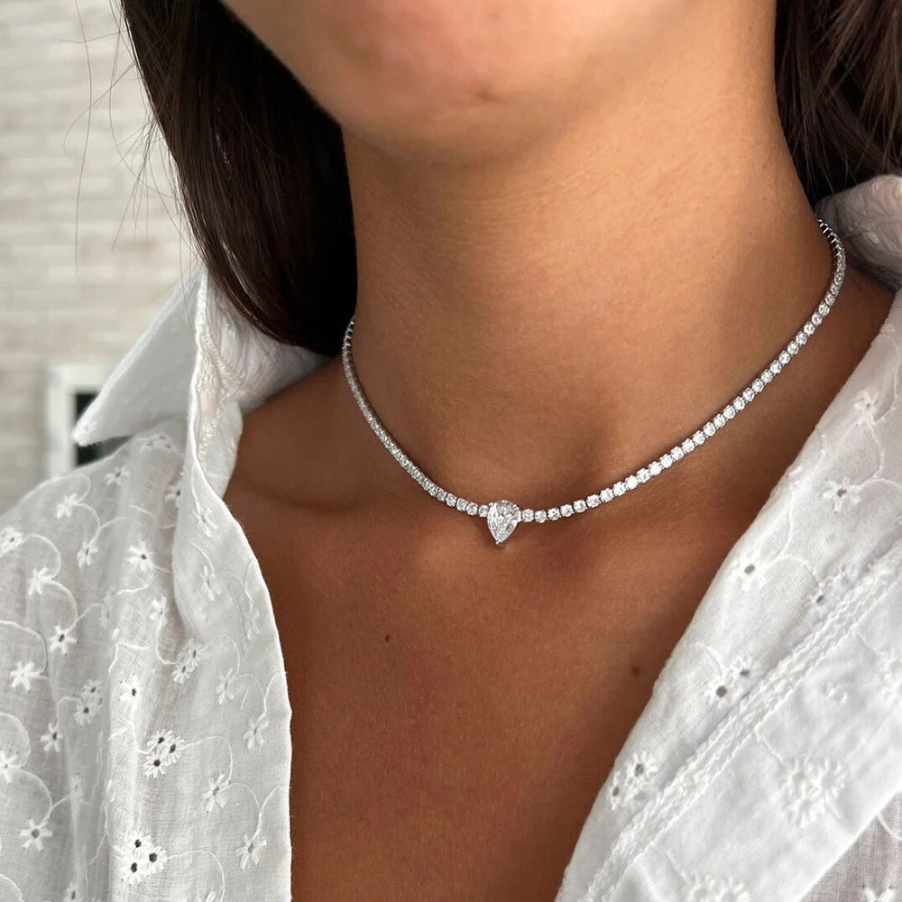 Necklace with a heart-shaped pendant worn by a person in a white blouse.
