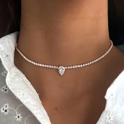 Diamond necklace with a heart-shaped pendant on a person wearing a white lace garment.