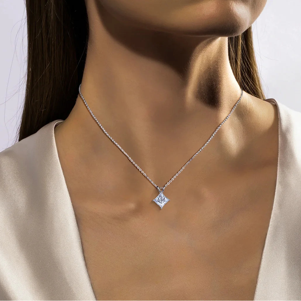 Close-up of a woman wearing a silver necklace with a diamond pendant against a neutral background