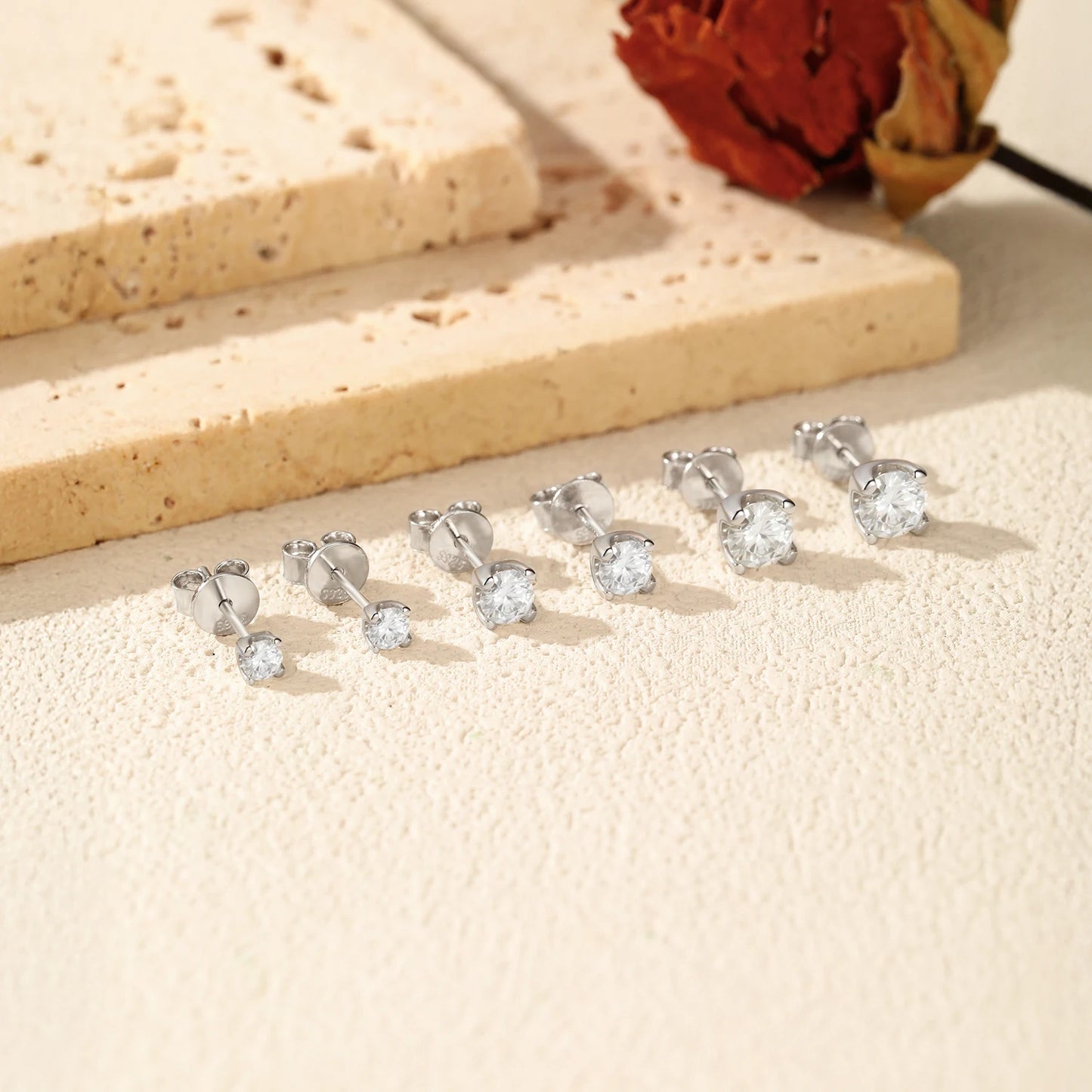 Silver stud earrings with clear gemstones on a beige surface.